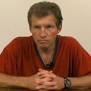 Unsmiling man with brown and gray hair wearing a red shirt